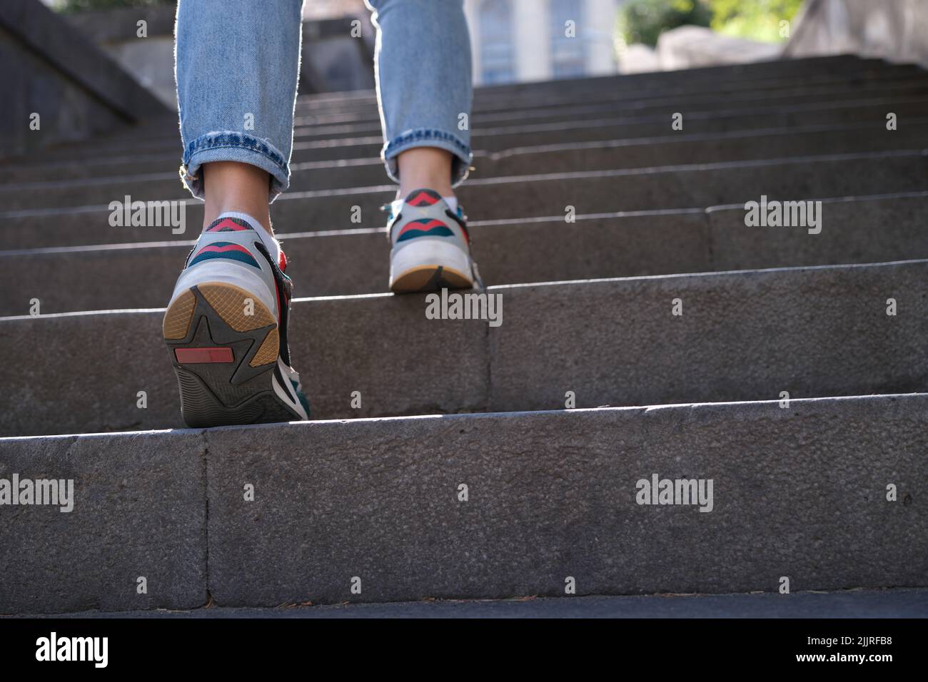 Frau in Jeans und Sneakers, die eine steile Treppe hinaufsteigt Stockfoto