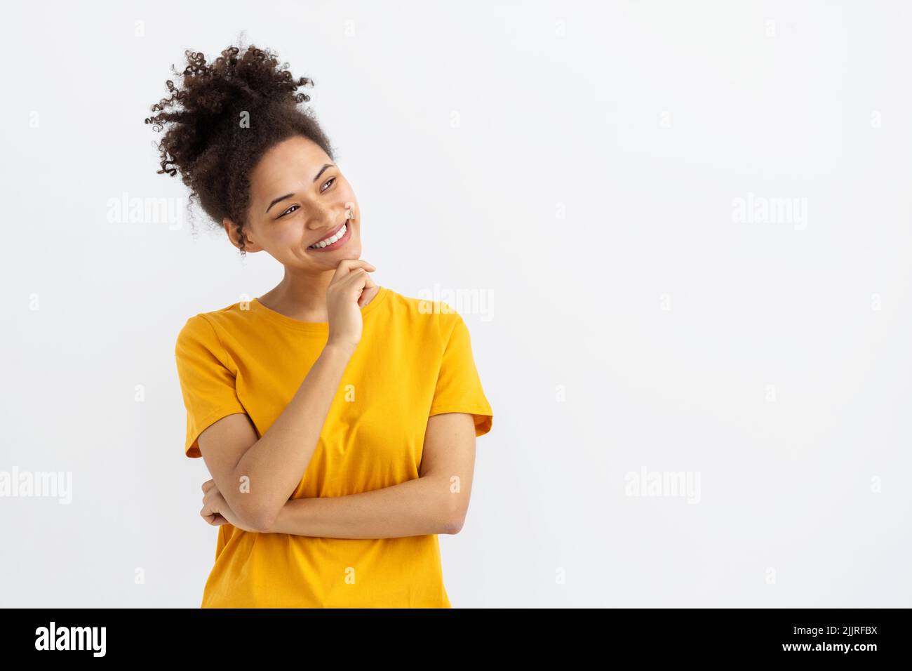 Porträt einer jungen Frau, die lächelt und auf einem weißen Hintergrund mit einem Kopierbereich wegschaut, lächelt freundlich Stockfoto