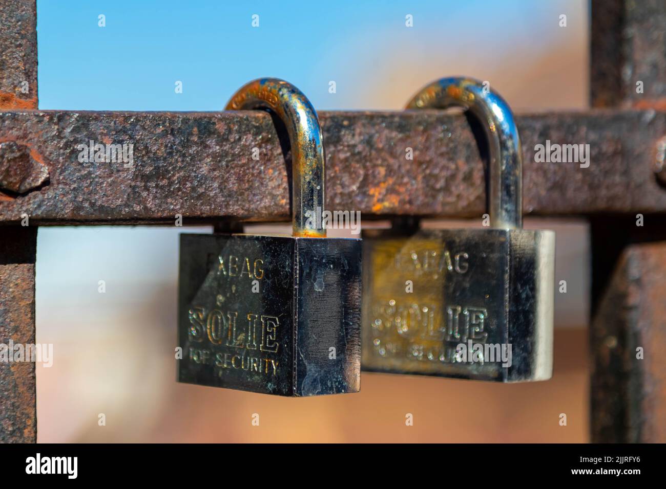 Eine Nahaufnahme von zwei silbernen geschlossenen Vorhängeschlössern, die auf dem rostigen Metallmast isoliert sind Stockfoto