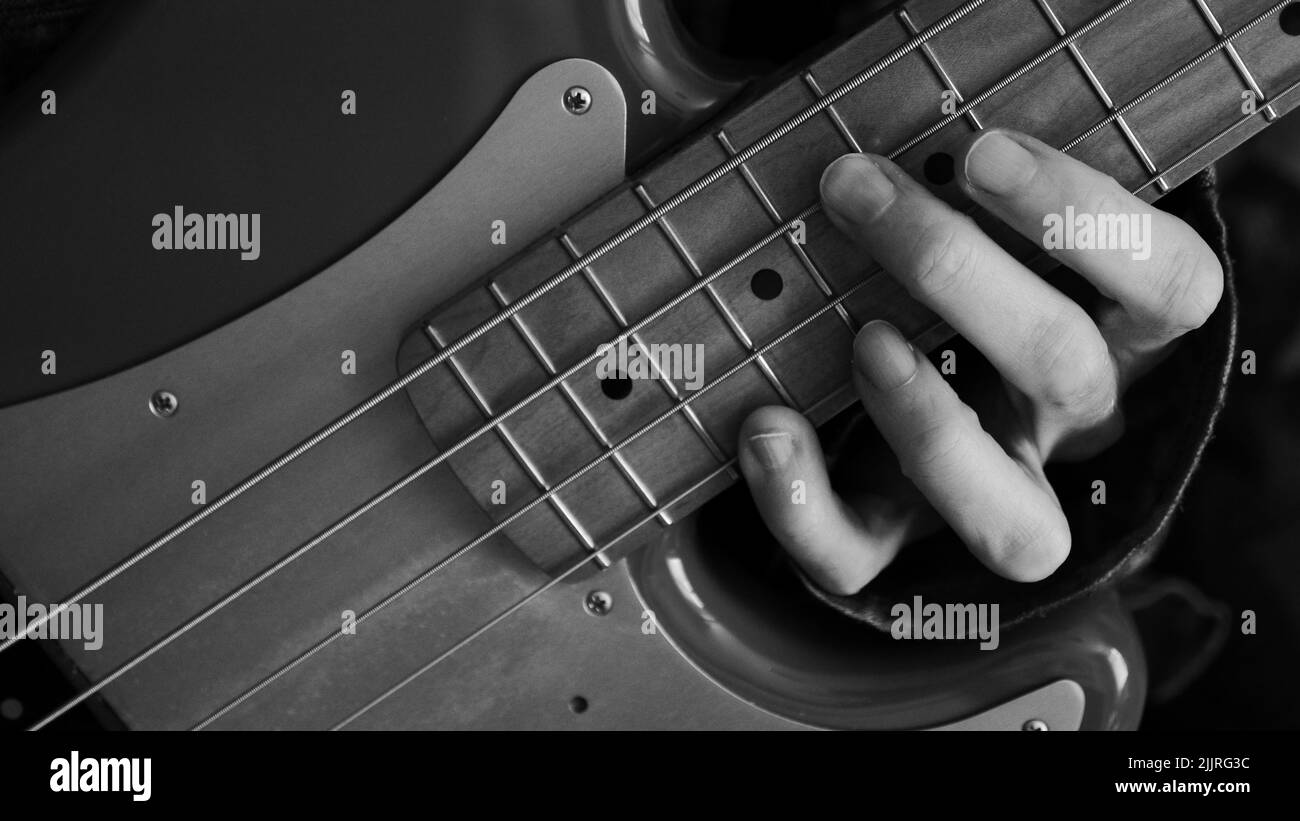 Eine Nahaufnahme Graustufen einer Hand, die einen Akkord auf der Bassgitarre hält - für Hintergründe Stockfoto