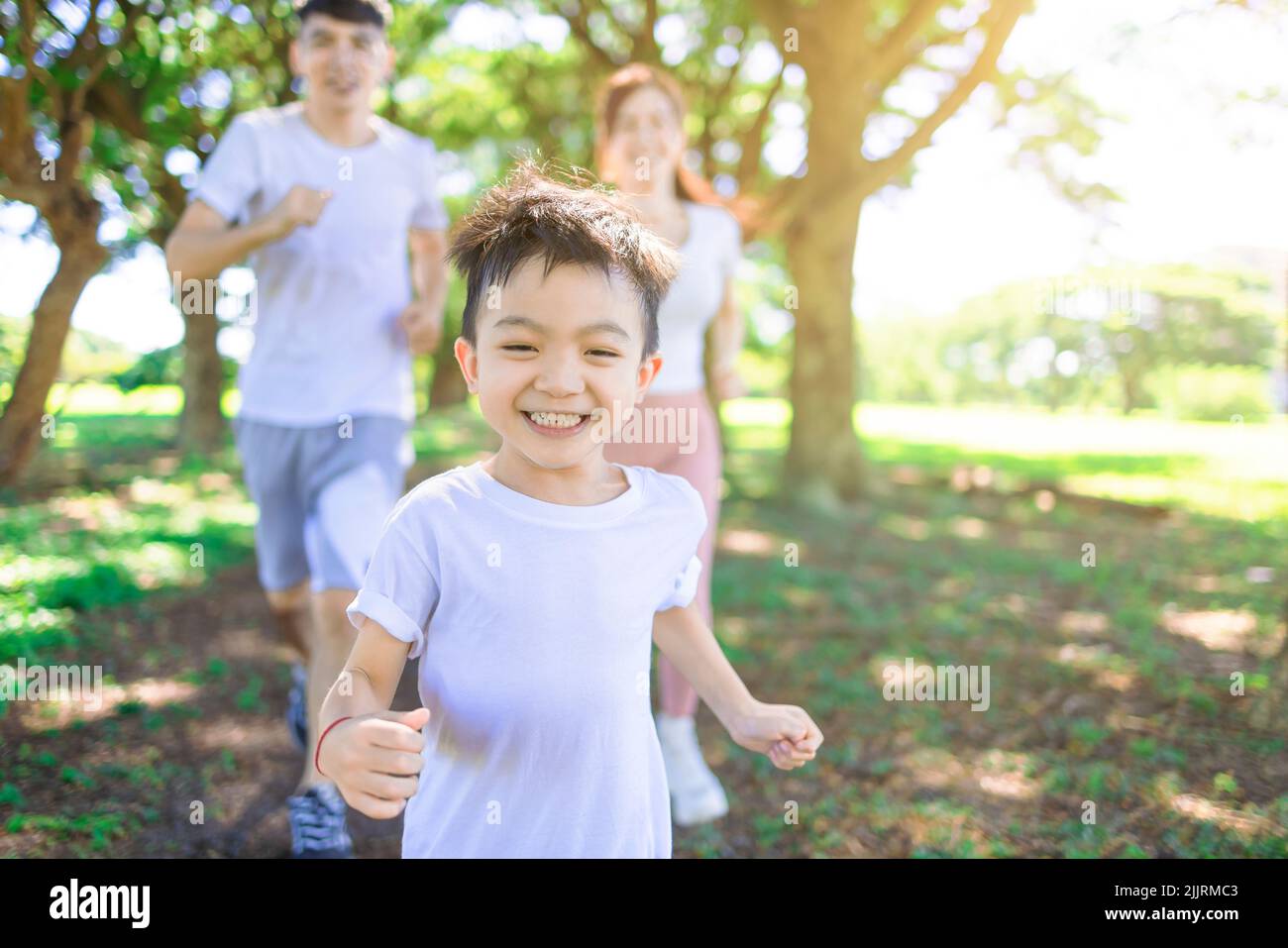 Fröhliches Kind beim Joggen mit den Eltern im Stadtpark Stockfoto