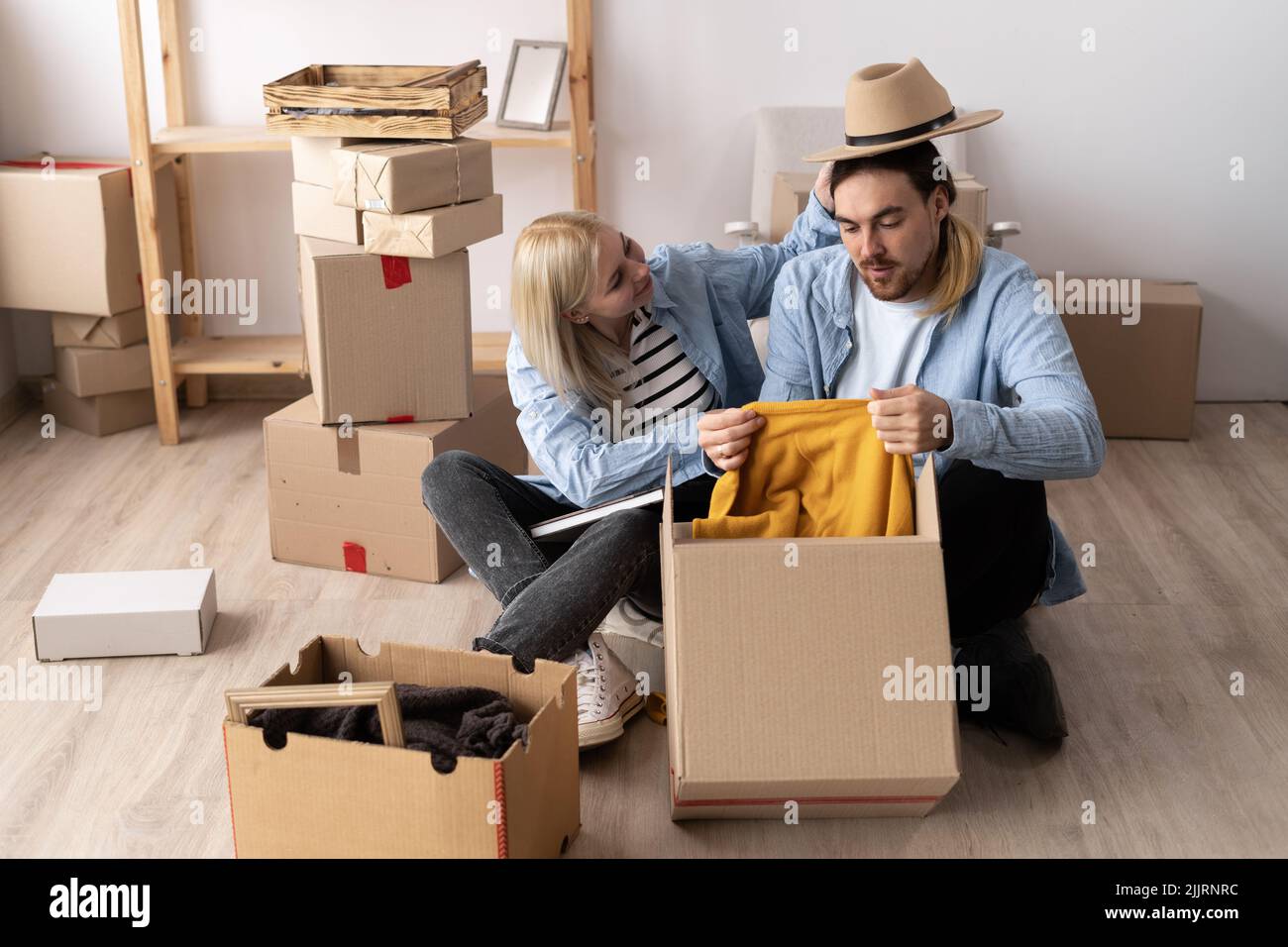 Junges Paar, das Boxen mit Sachen und Kleidung auspackt, zieht in ein neues Haus, neue Wohnungseigentümer sitzen auf dem Boden mit Kästen, glückliche bewegende Zeit Stockfoto