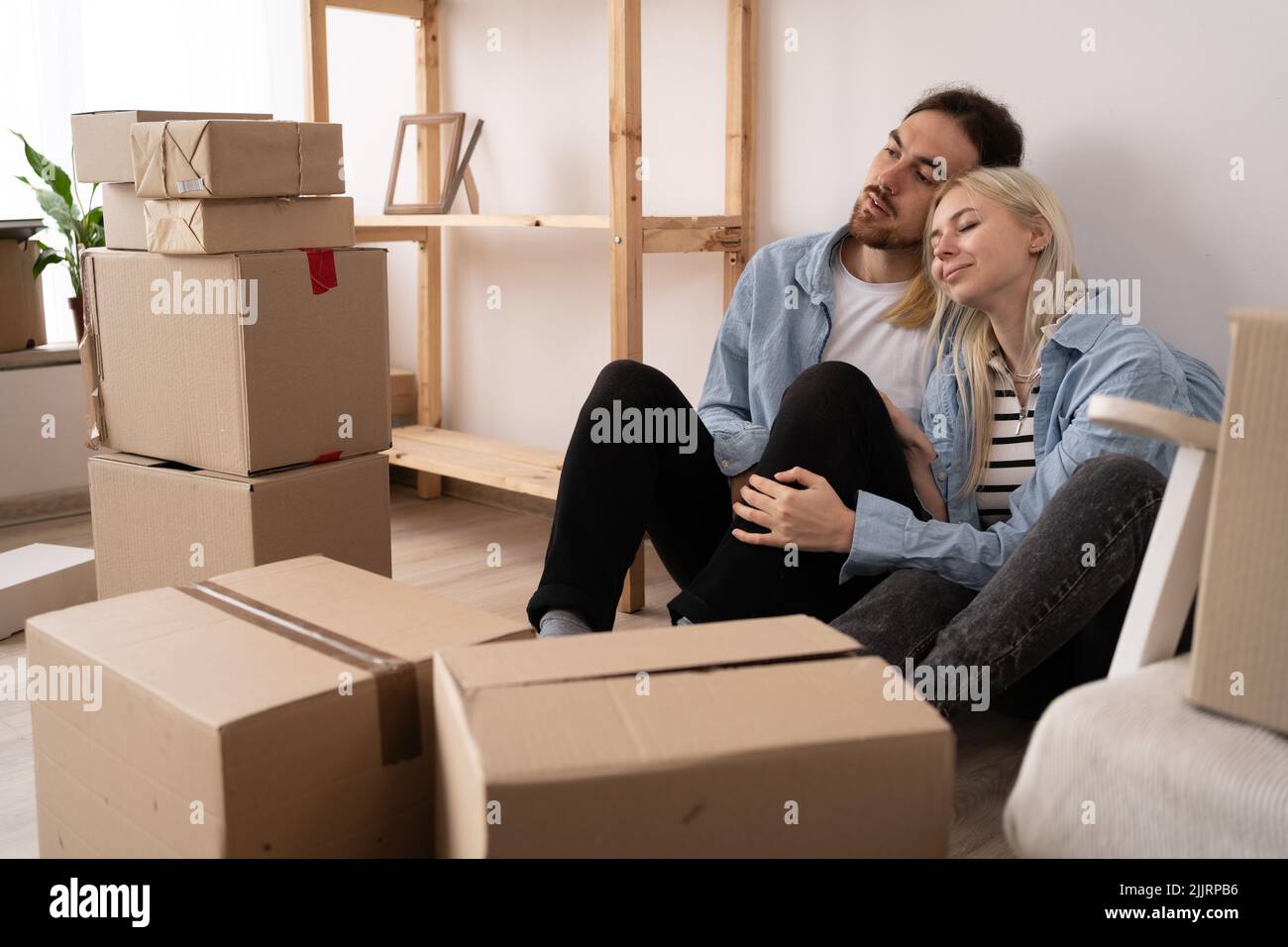 Glückliches junges Paar, das nach dem Umzug auf dem Boden in einer neuen Wohnung sitzt Stockfoto