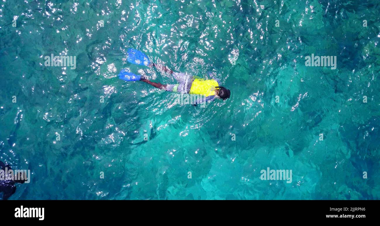 Ein Blick von oben auf einen Mann, der in türkisfarbenem Wasser mit Korallenriff auf den Malediven schwimmend ist Stockfoto