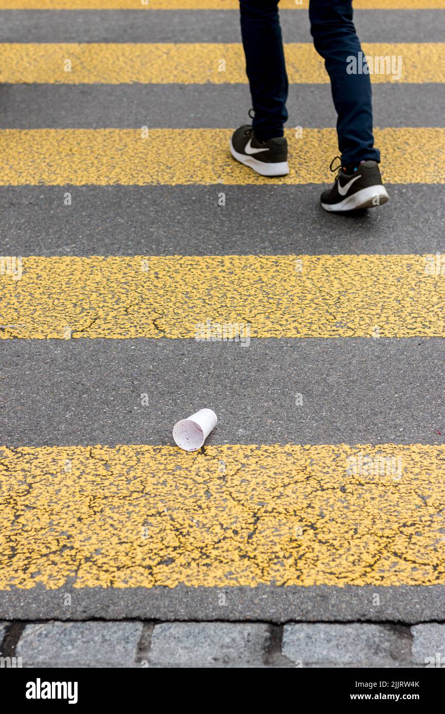 Eine vertikale Aufnahme eines Crosswalks und eines Mannes, der in Nike Schuhen und einem weißen Plastikbecher vorbeikommt Stockfoto