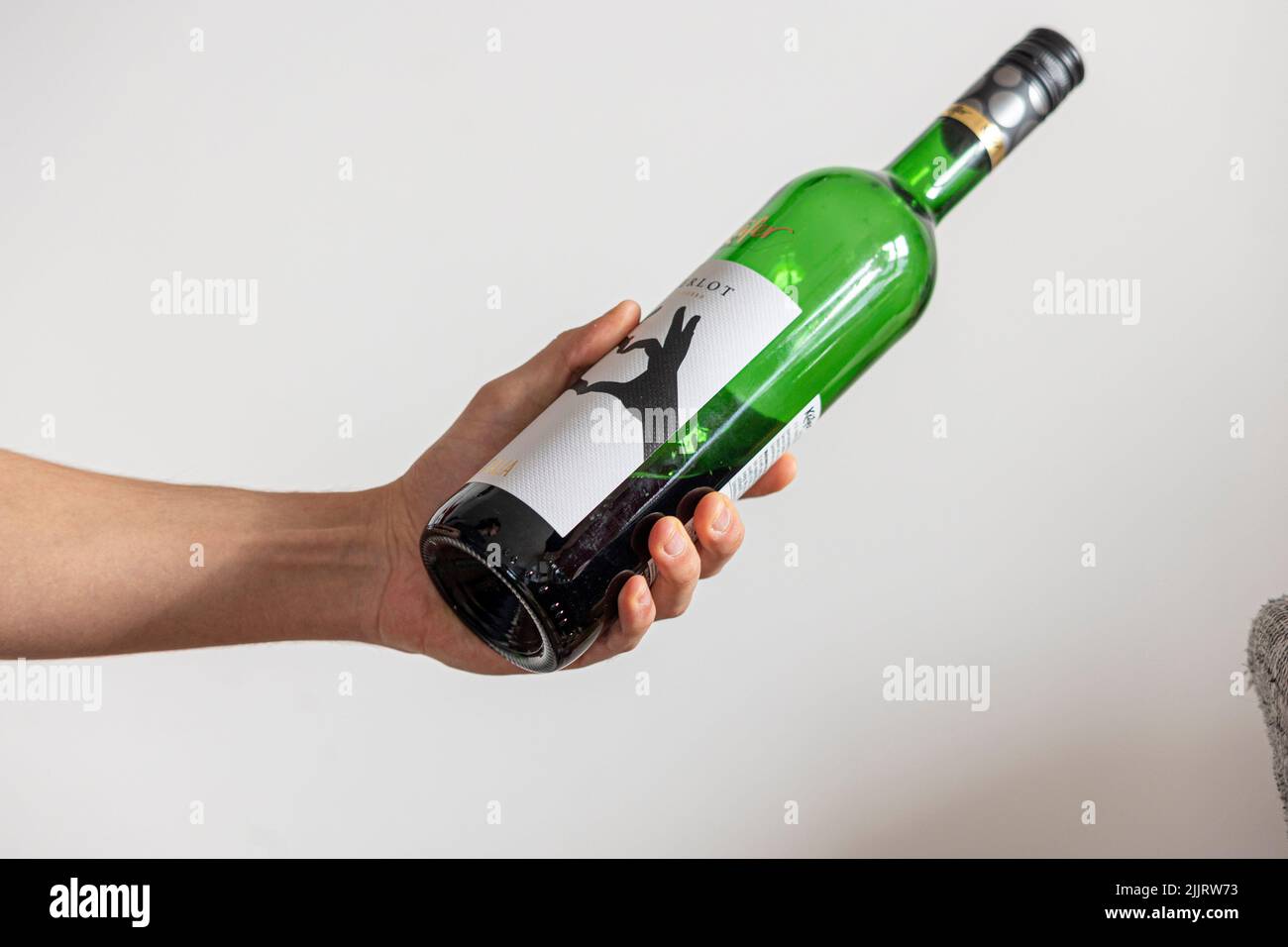 Eine Nahaufnahme einer Weinflasche und eine Hand, die sie gegen die weiße Wand hält Stockfoto