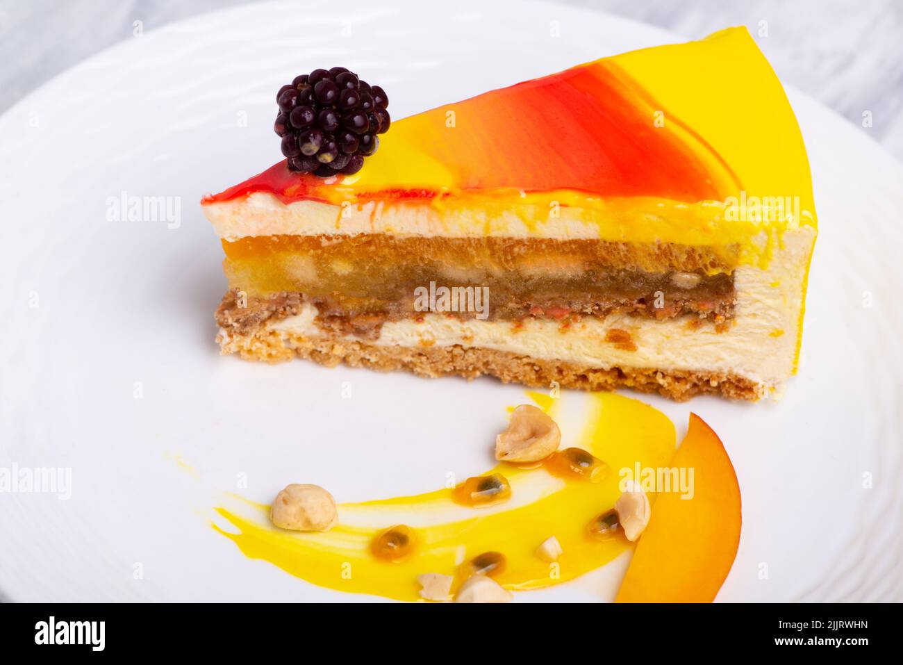 Eine Nahaufnahme einer kleinen Brombeere auf einer Mango-Mousse-Kuchenscheibe auf einem weißen Teller Stockfoto