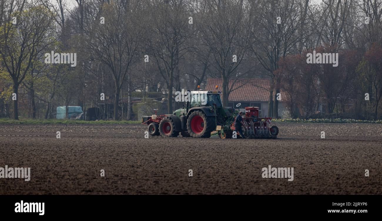 Eine schöne Aufnahme eines Mannes, der einen Fendt-Traktor beim Pflügen auf einem landwirtschaftlichen Feld in Nederweert, Niederlande, gewartet hat Stockfoto