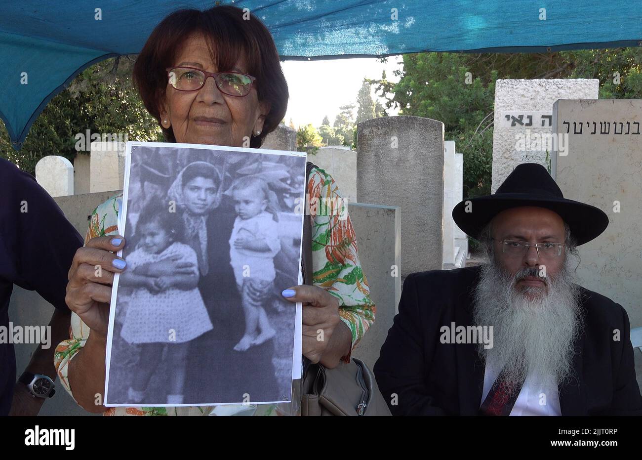 GIVATAYIM, ISRAEL - JULI 27: Ruth Sharabi, die Schwester von Yosef Melamed, einem jemenitischen Kind, das 1949 starb, Zeigt ein Kinderbild, das sie und Yossef mit ihrer Mutter zeigt, wie israelische medizinische Anthropologen das Grab des Kindes exhumieren, um am 27. Juli 2022 in Givatayim, Israel, eine DNA-Probe auf dem Friedhof von Nahalat Yitzhak zu entnehmen. Das Grab wurde geöffnet, um der Familie des Jungen zu beweisen, dass er dort begraben ist und nicht entführt und zur Adoption aufgelegt wurde. In den 1950s Jahren in Israel verschwanden jemenitische Kinder, deren Eltern behaupteten, sie seien „entführt“ worden. Kredit: Eddie Gerald/Alamy Live Nachrichten Stockfoto
