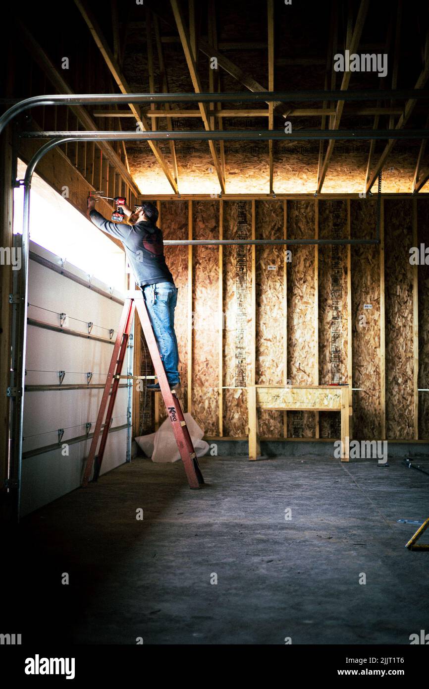 Eine vertikale Aufnahme eines Bauarbeiters, der einen letzten Schliff an ein Garagentor setzt Stockfoto