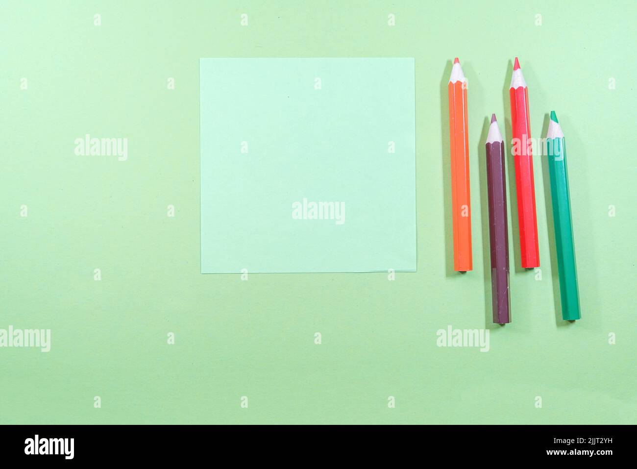 Eine Draufsicht auf Minze-Haftnotizen mit Copyspace neben bunten Bleistiften auf hellgrünem Hintergrund Stockfoto