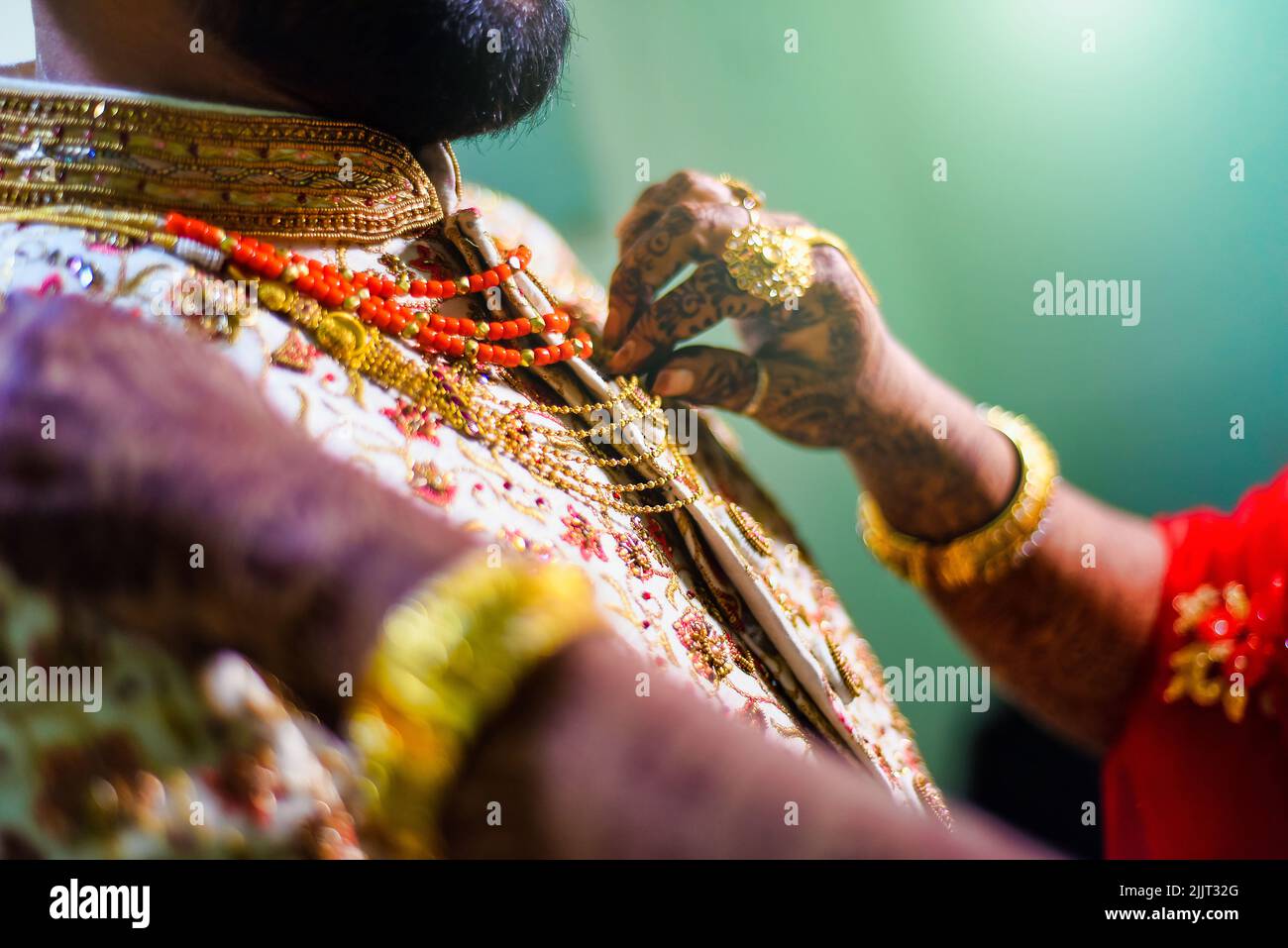 Eine Nahaufnahme von gesichtslosen Fingern einer Frau, die die Accessoires auf den Sherwani des Bräutigams fixieren Stockfoto
