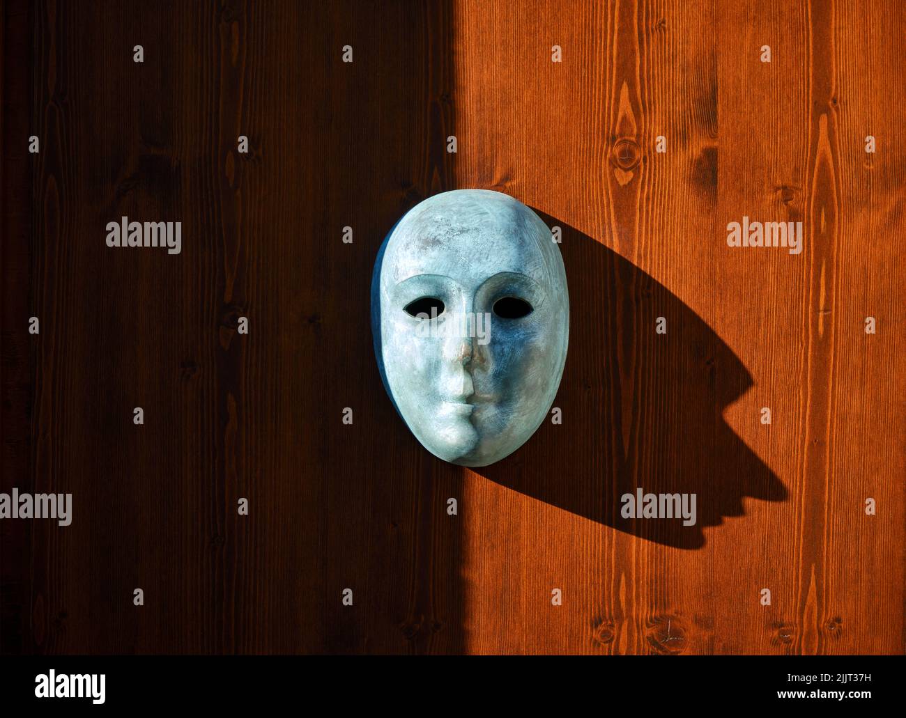 Venezianische Maske auf Holzhintergrund mit kontrastreichen Schatten, Vorderansicht buntes Bild Stockfoto