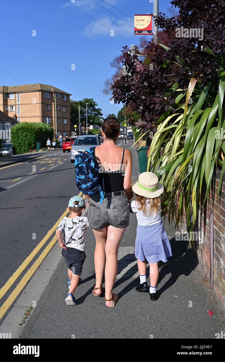 Junge Mutter und zwei kleine Kinder, die auf dem Bürgersteig in Großbritannien zur Schule gehen Stockfoto