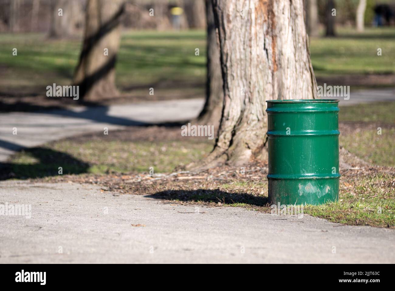 Ein grüner Metallabfallbehälter am Fuße eines Baumes im Park Stockfoto