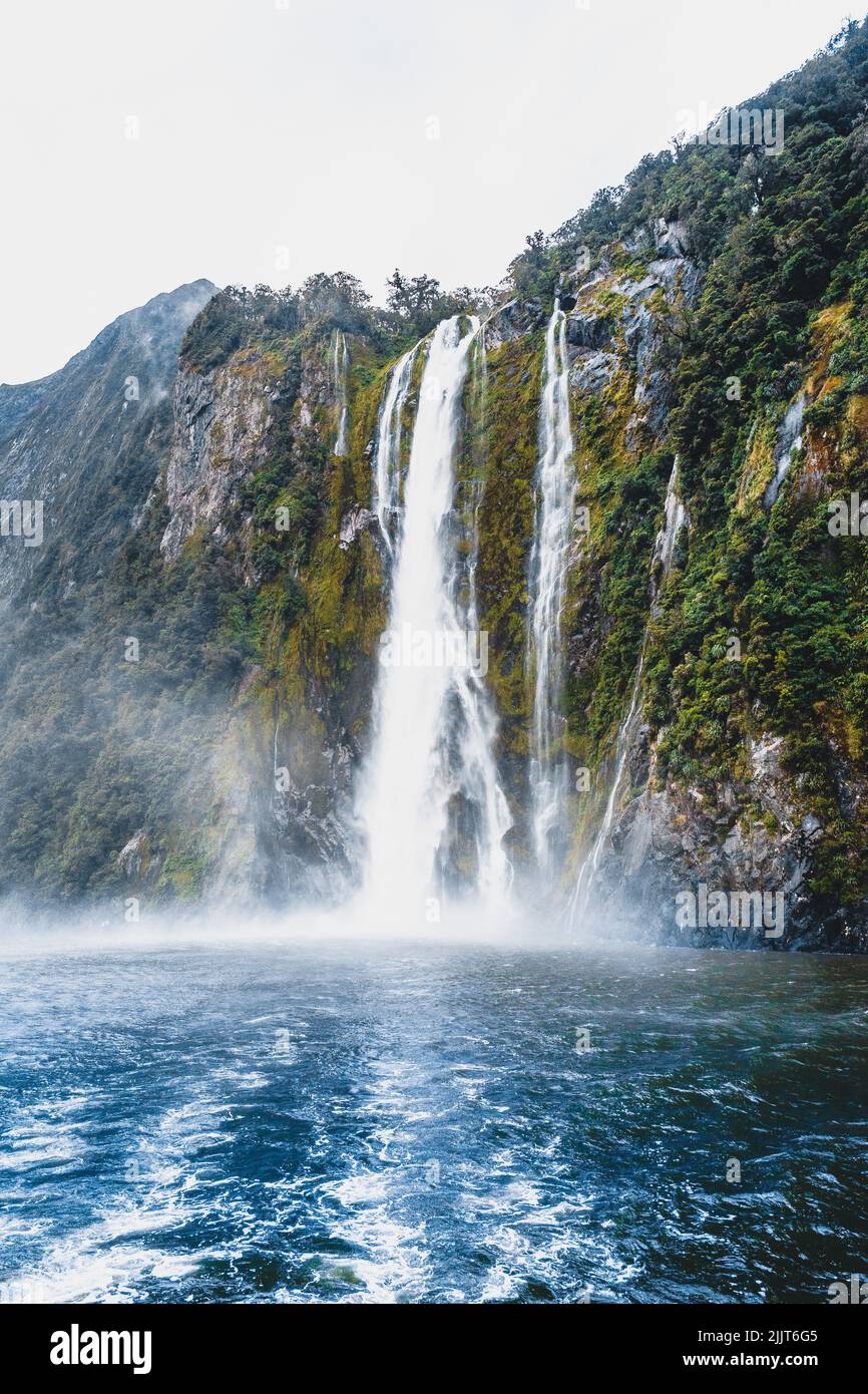 Eine wunderschöne vertikale Aufnahme eines Wasserfalls über einem frischen Teich, umgeben von üppigem Grün in den Milford Sounds in Neuseeland Stockfoto