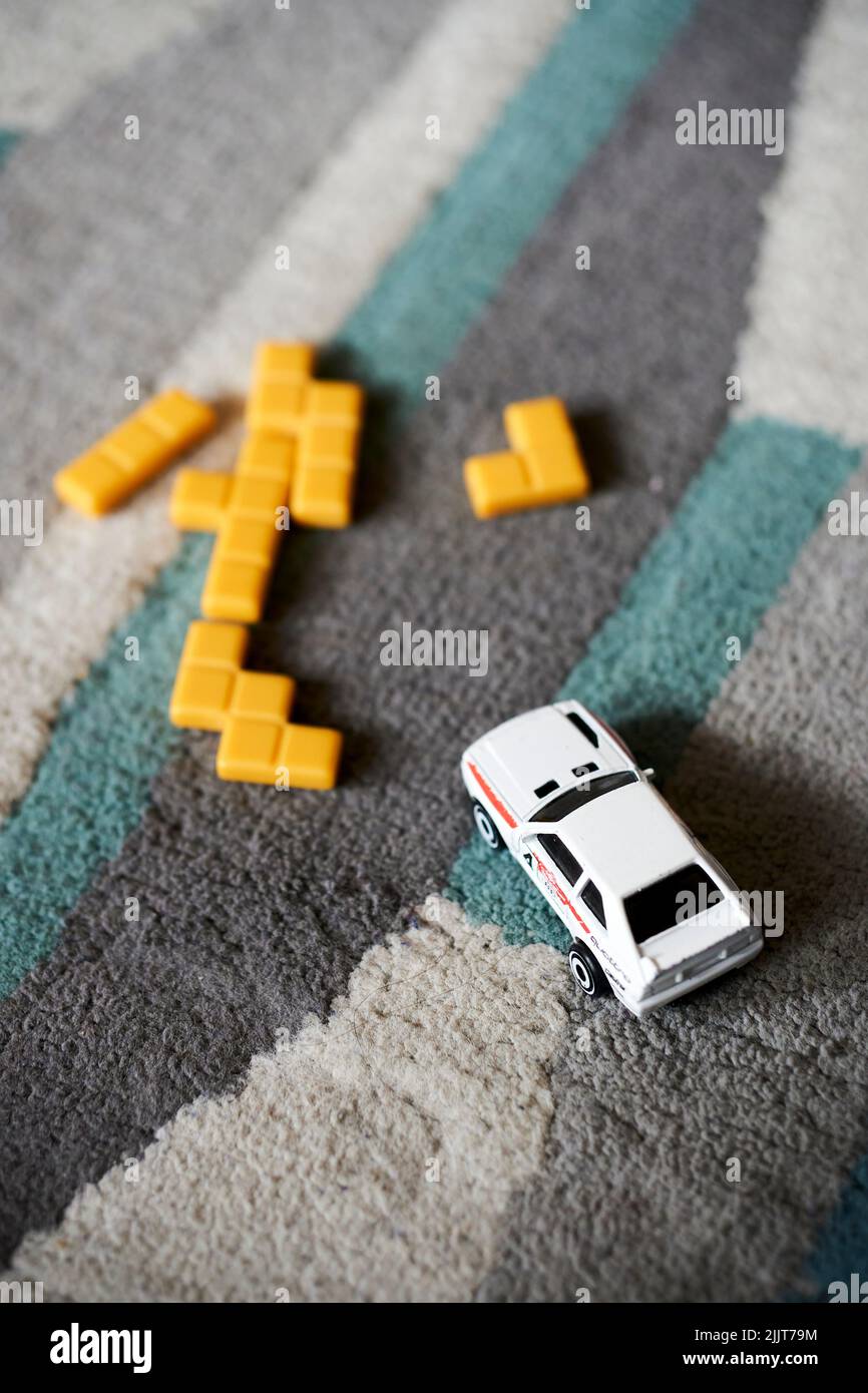 Ein Nahaufnahme weißes Mattel Hot Wheels Spielzeug-Modellauto und gelbe Spielfliesen auf einem Teppichboden. Stockfoto