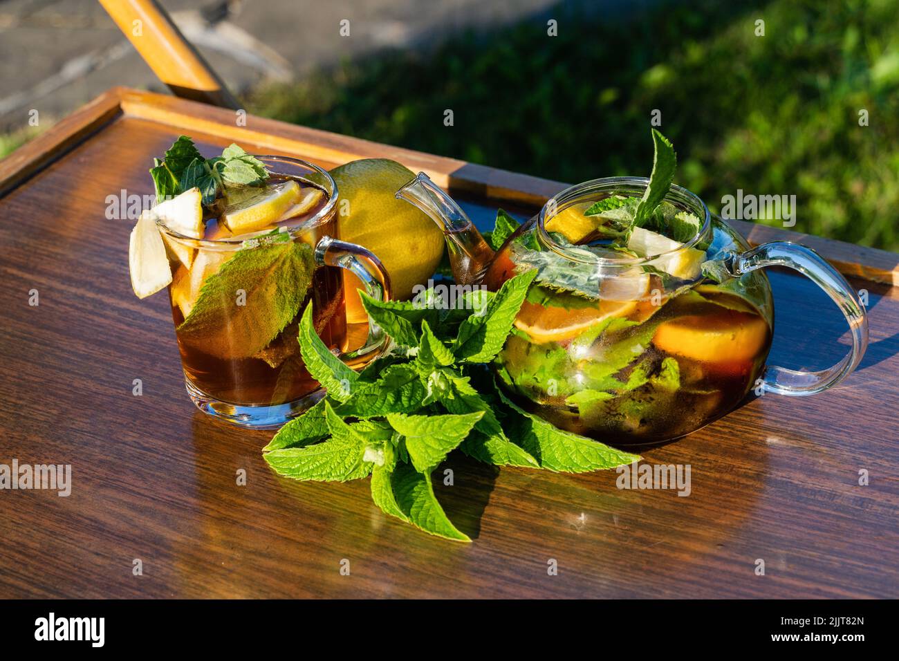 Glas Teekannen mit Minze und Zitrone und Tasse in einem Garten des Landhauses, Sommertag. Stockfoto