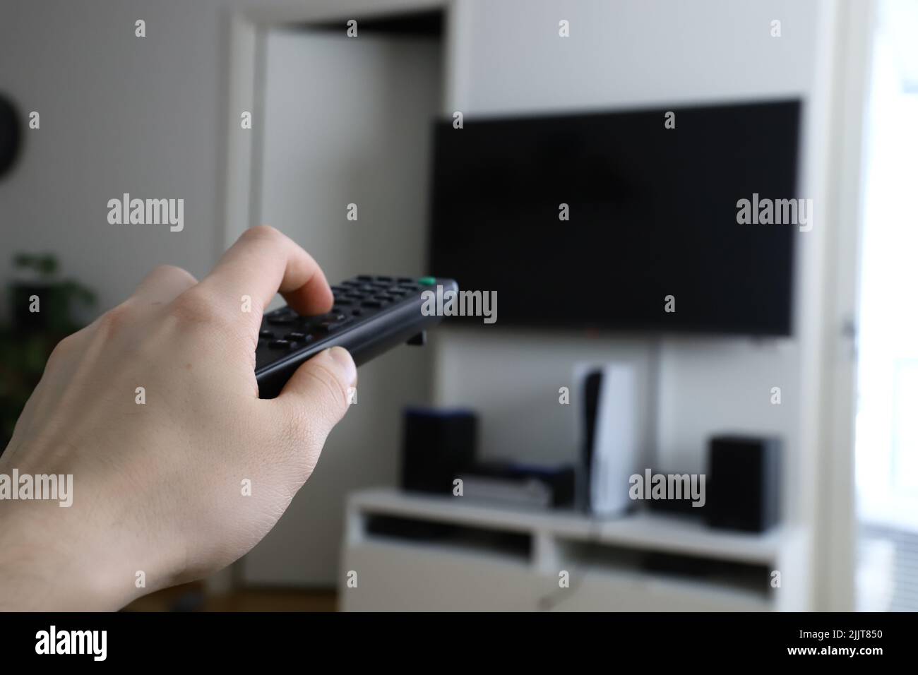 Die Hand eines Mannes, der eine Fernbedienung hält, zeigt auf den Fernseher Stockfoto