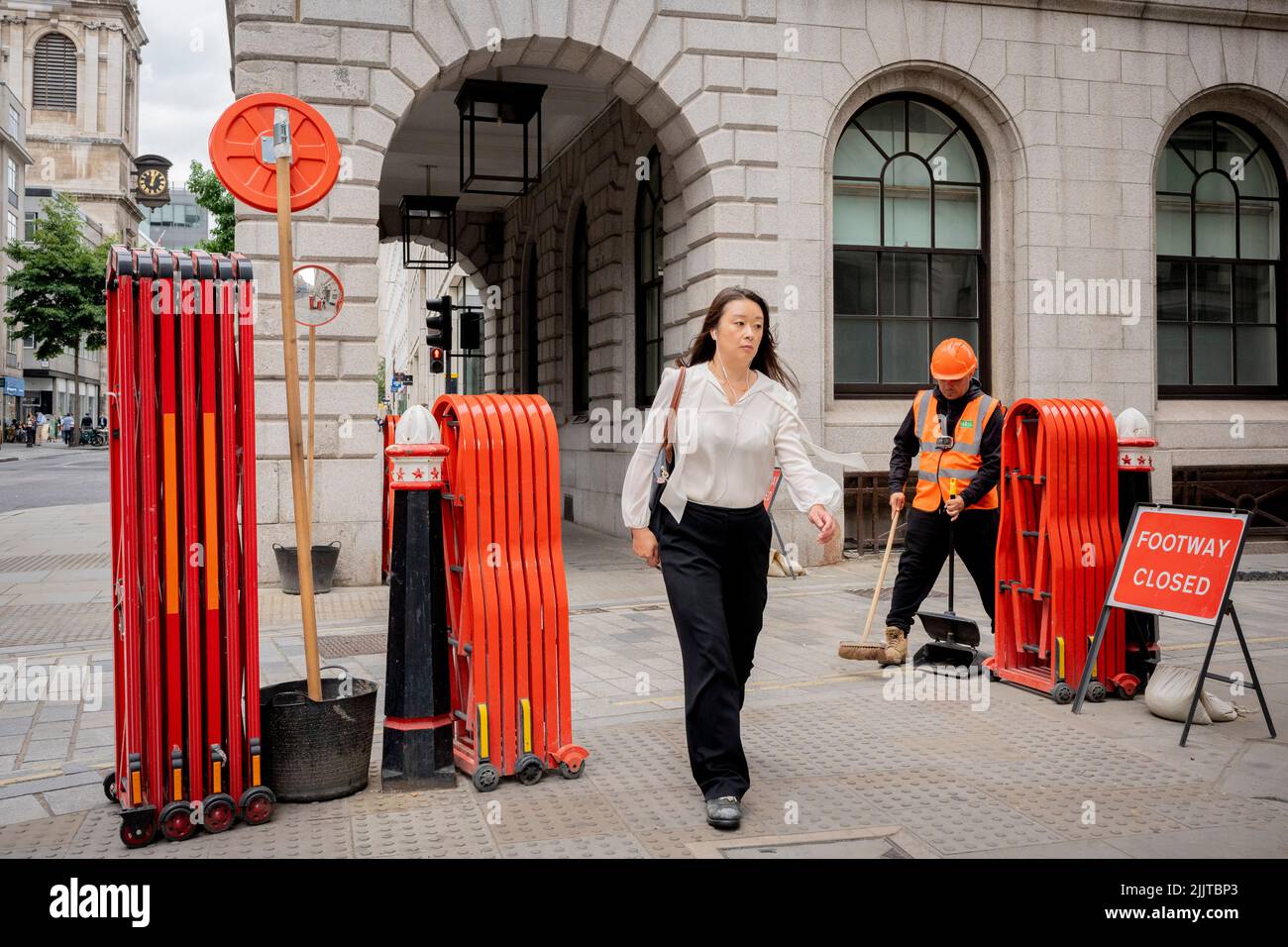 Fußgänger gehen zwischen den auf dem Bürgersteig befindlichen Ziehharmonika-Turtle-Gates, die von Banksmen während der Bauarbeiten in der City of London, dem Finanzdistrikt der Hauptstadt, am 27.. Juli 2022 in London, England, entfaltet werden können. Stockfoto