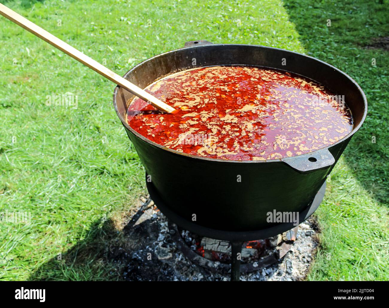 Eine Nahaufnahme einer Gulaschsuppe in einem großen gusseisernen Topf, die auf einem Lagerfeuer im Freien kocht Stockfoto