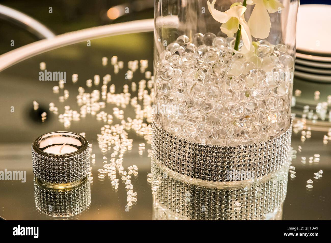 Eine Nahaufnahme einer glänzenden Glasflasche mit kleinen Kugeln und einer Kerze auf einem Tisch Stockfoto