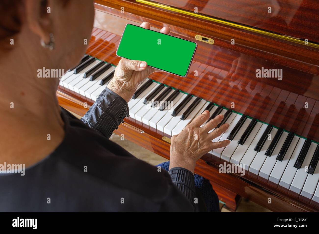 Die alte Frau spielt Klavier, schaut in die Telefonnotizen. Chroma-Taste auf dem Smartphone Stockfoto
