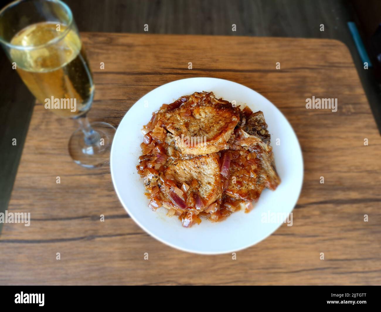 Eine Nahaufnahme von geschmorten Schweinekoteletts auf einem weißen Teller neben einem Glas Champagner auf einem Holztisch Stockfoto