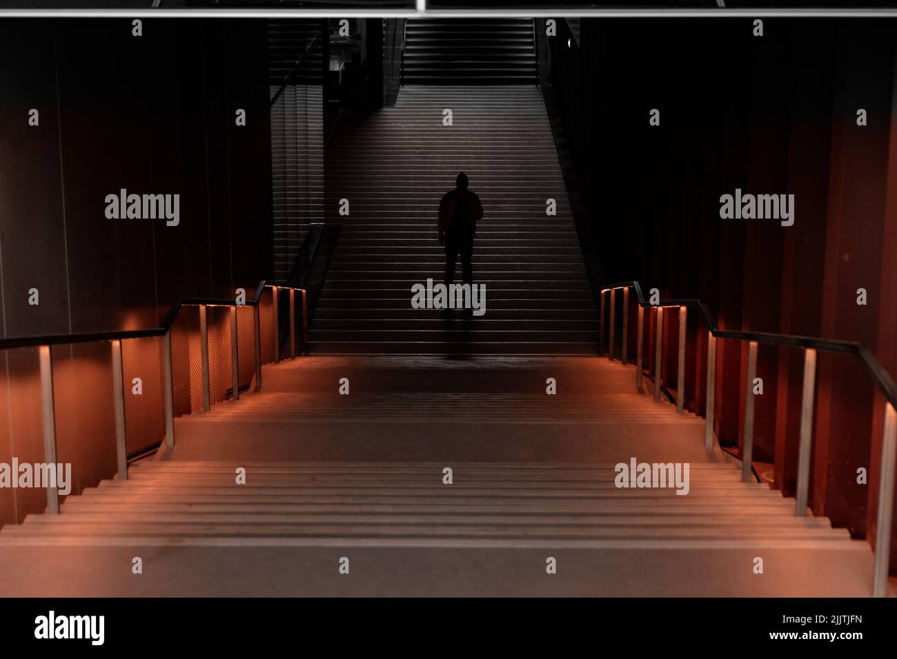 Eine Silhouette eines Mannes, der allein in der Mitte eines unterirdischen Tunnels zwischen den Treppen steht Stockfoto