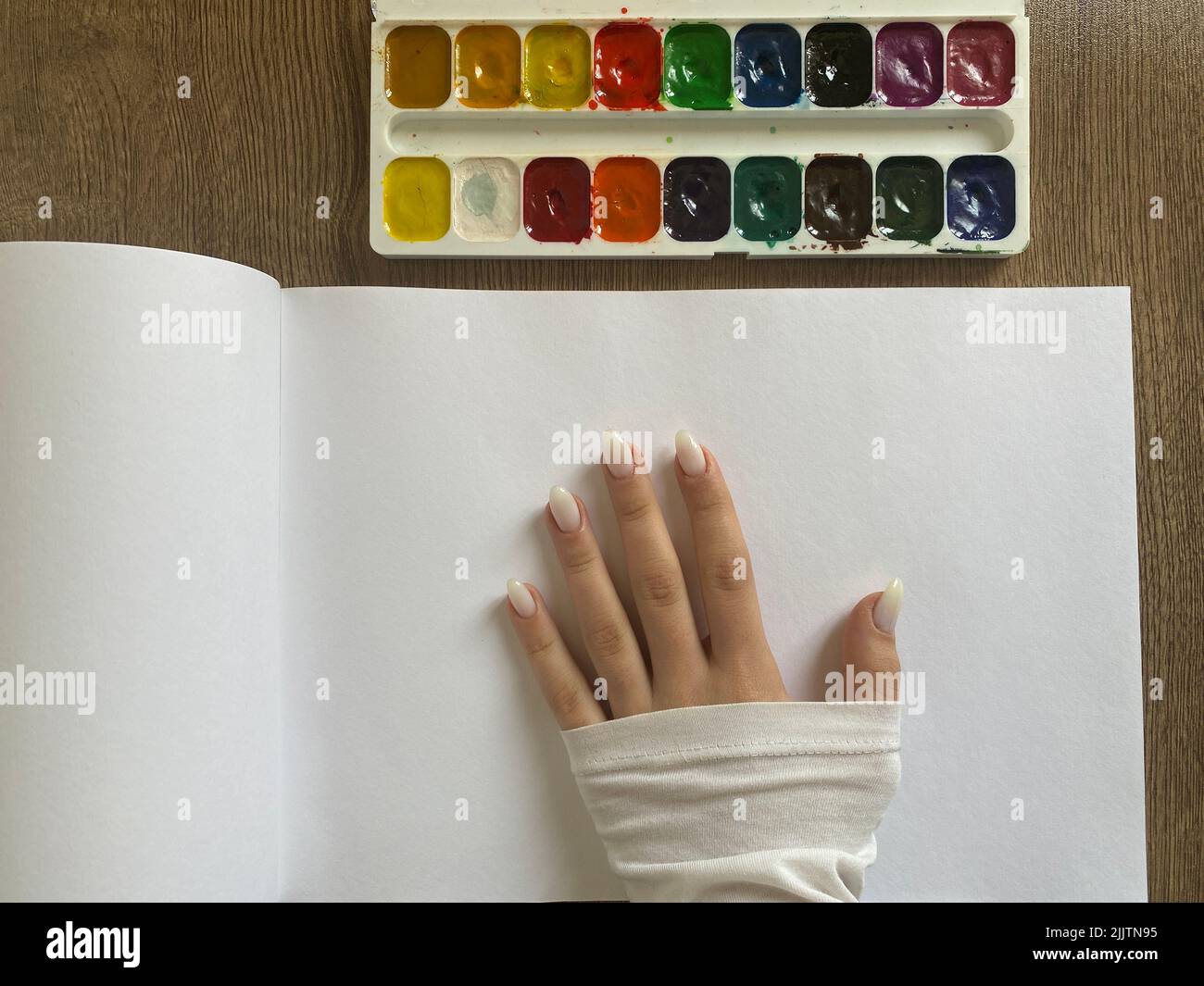 Eine Hand auf einer weißen Albumseite und Aquarell auf einem Holztisch Stockfoto
