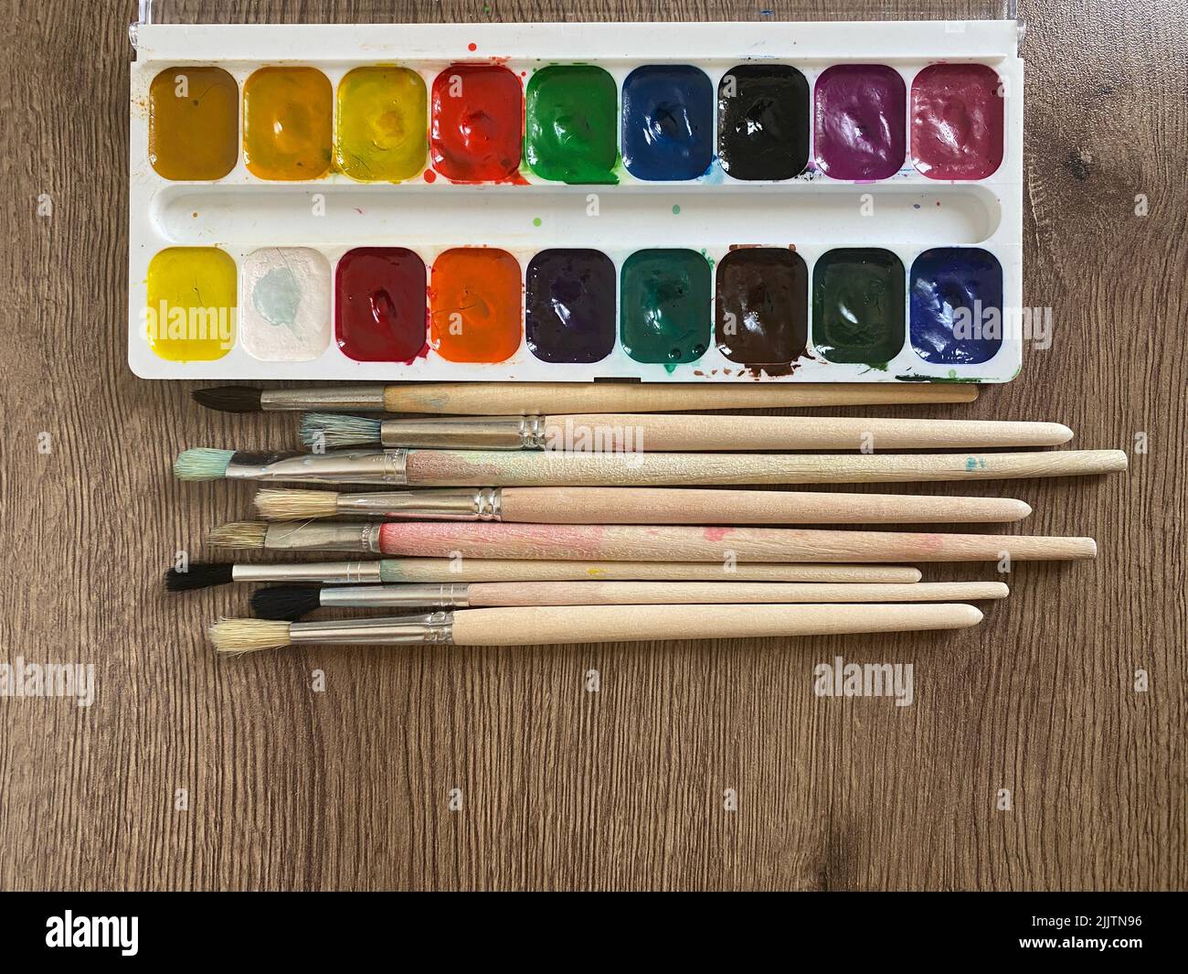 Eine Reihe verschiedener Pinsel und Aquarellfarben auf einer hölzernen Oberfläche Stockfoto