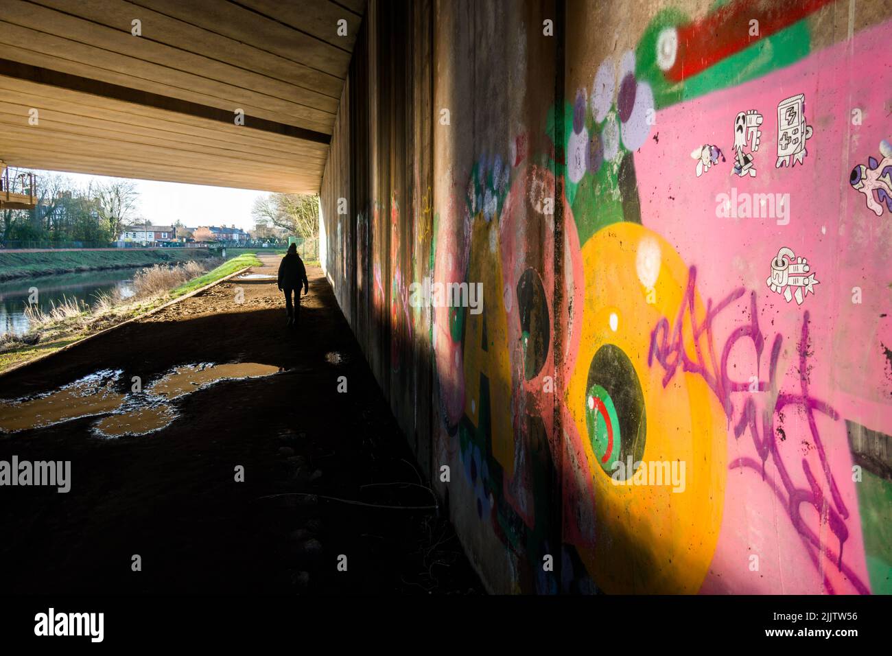 Eine schattige Figur in einer Autobahnunterführung mit Graffiti an bunten Wänden Stockfoto