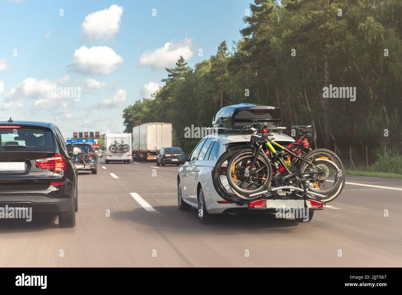 Rückansicht moderner weißer Familienwaggon mit montiertem Dachkoffer-Kofferraum und Fahrradträger, der die europäische Autobahn gegen den blauen Himmel am Sommertag fährt Stockfoto