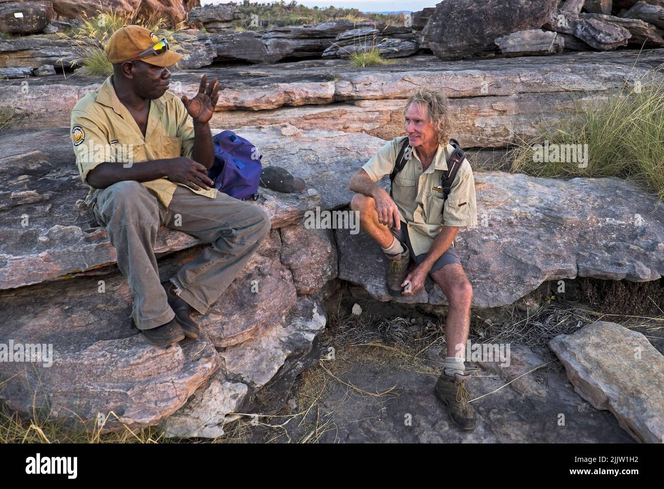 Einheimische und weiße Reiseleiter tauschen sich bei Sonnenuntergang auf dem Gipfel des Ubirr Rock im Kakadu National Park im Northern Territory aus. Der einheimische Führer James Dempsey arbeitet für die Njanjma Rangers (https://www.facebook.com/media/set/?set=a.712004628855859.1073741862.143141119075549&type=1). Sein Kollege, der formr Pressefotograf, Robert McKell, ist bei Kimberley Wild angestellt. Stockfoto