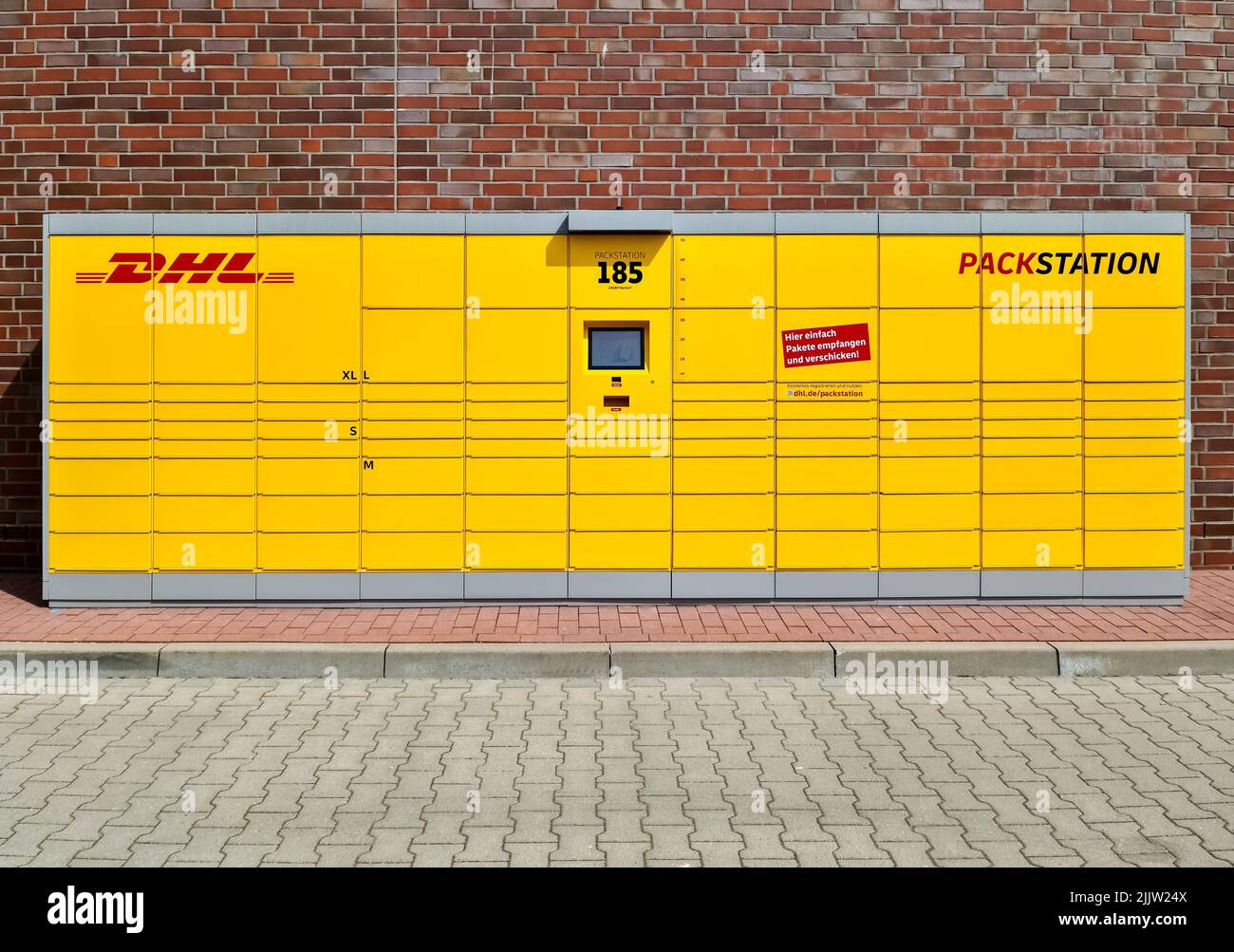 Eine gelbe Paketstation des deutschen Paketdienstes DHL vor einer Ziegelwand Stockfoto