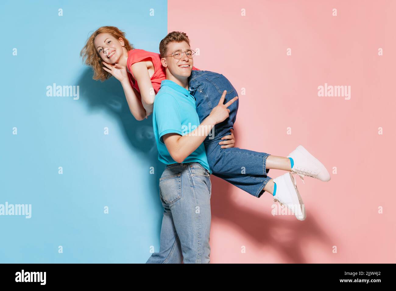 Porträt eines fröhlichen jungen Paares, posiert, Mann trägt Frau auf seiner Schulter isoliert über rosa blauen Studio-Hintergrund Stockfoto