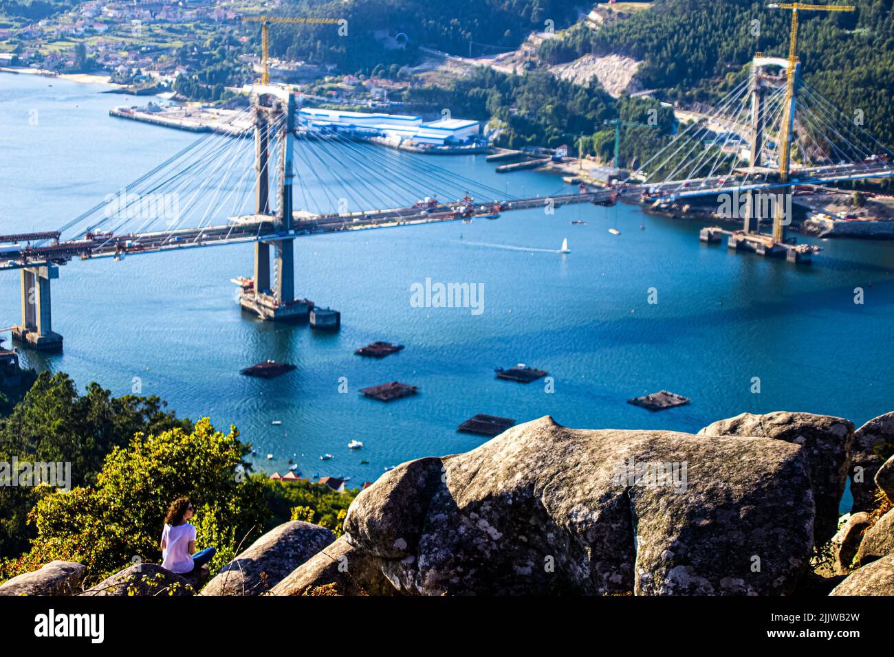 Ein Mädchen auf einem Hügel bewundert die wunderschöne Aussicht auf die Brücke von Rande und die Mündung in Vigo, Galicien Stockfoto