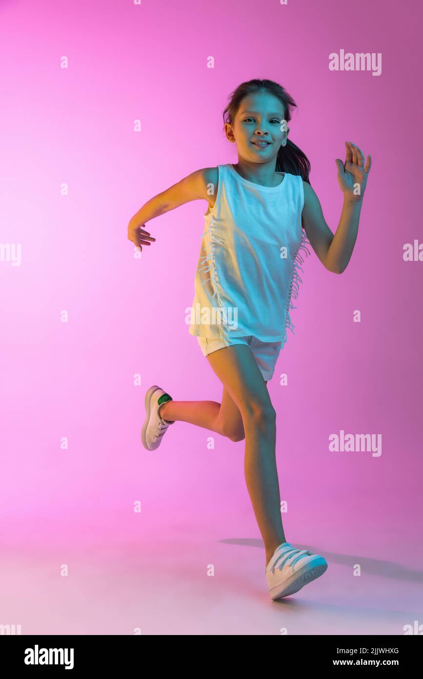 Happy Little schönes Mädchen, Schulmädchen in lässigem Outfit isoliert auf rosa Hintergrund in Neon. Konzept der Kinder Emotionen, Mode, Schönheit, ad Stockfoto