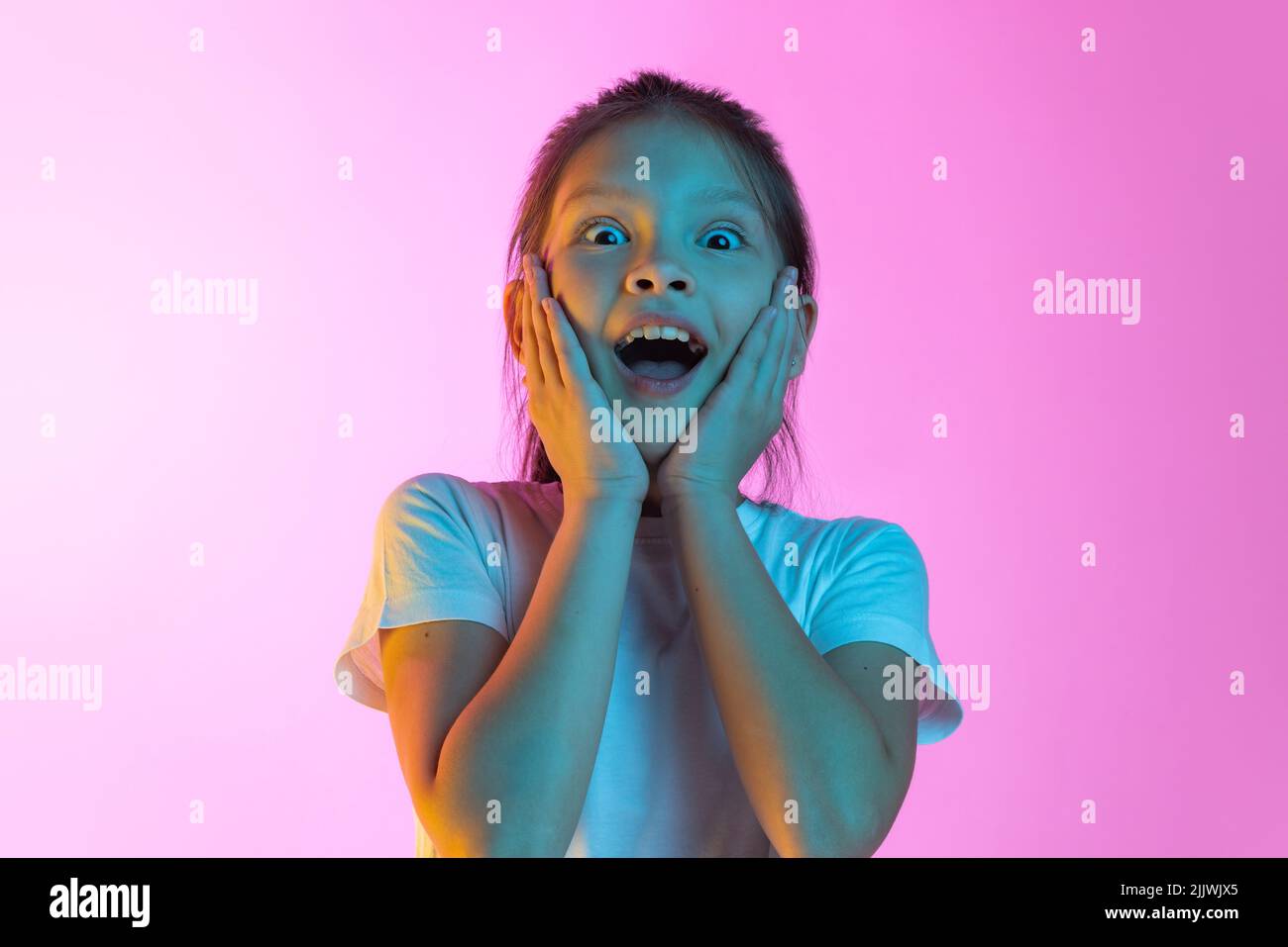 Überrascht kleine charmante Mädchen, Kind Blick auf die Kamera mit offenem Mund isoliert auf rosa Hintergrund in Neon. Konzept der Kinder Emotionen, Mode Stockfoto
