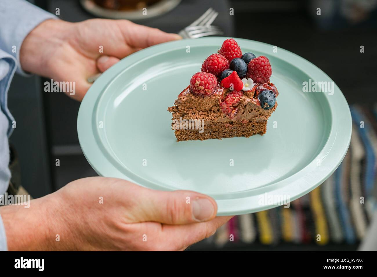 Eine grüne Platte aus Schokoladenmousse Kuchen Scheibe mit Beeren und Erdbeere in den Händen Stockfoto