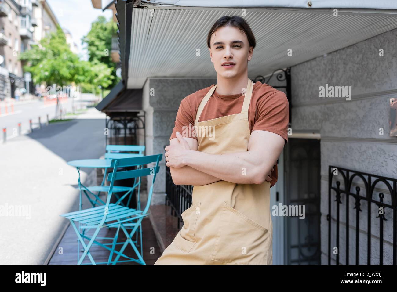 Junger Verkäufer in Schürze, der Arme auf der Terrasse von Süßwaren kreuzt Stockfoto