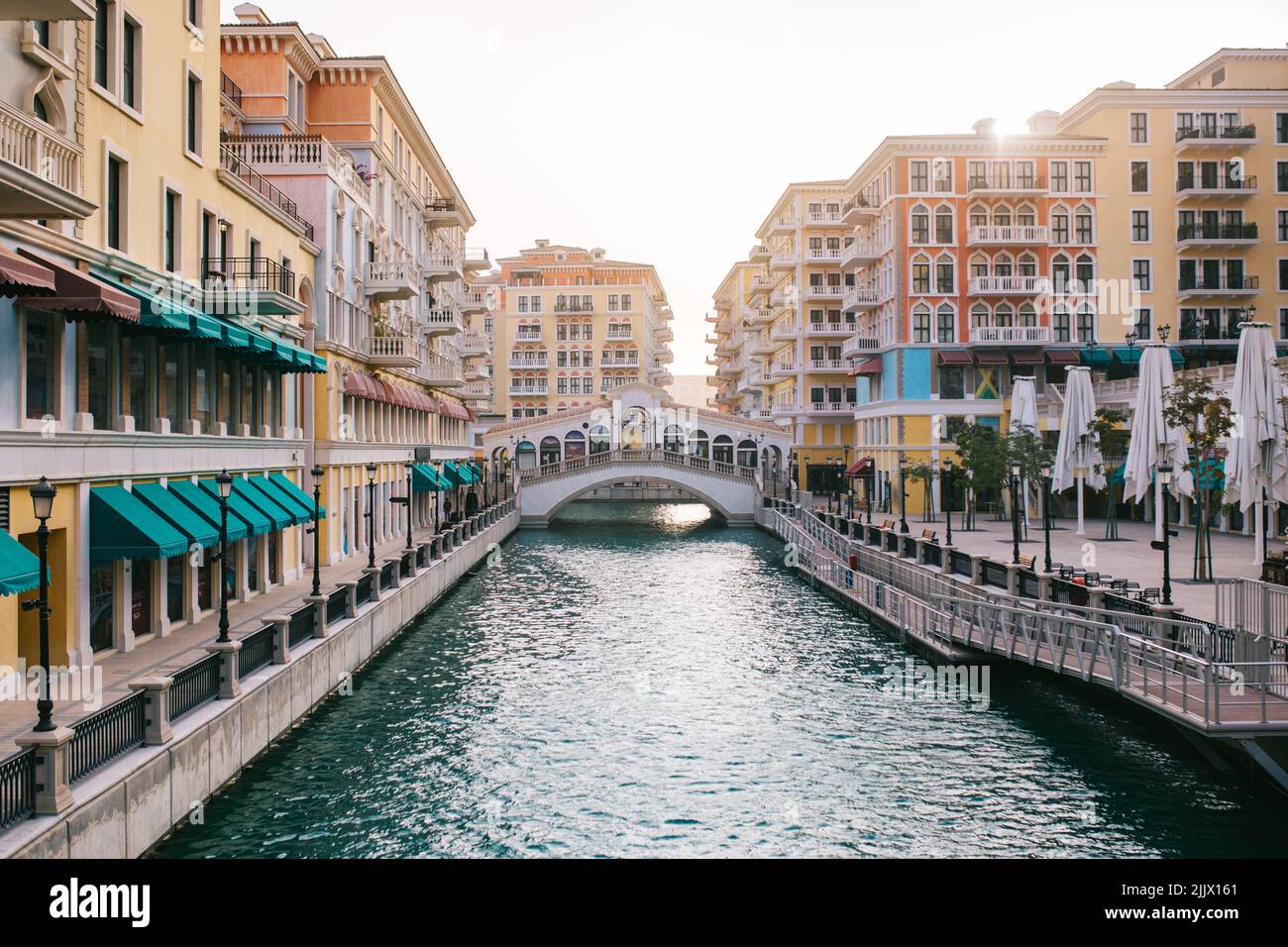 Farbenfrohe Häuser und Kanäle mit plätscherndem Wasser und einer Brücke, die sich am Morgen gegen den Sonnenaufgangshimmel auf der Straße von Doha, Katar, befindet Stockfoto