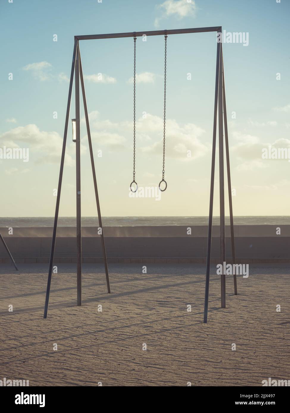 Zwei Gymnastikringe, die am frühen Morgen in Los Angeles, USA, an der Bar gegen den bewölkten Sonnenaufgangshimmel am sandigen Venice Beach hängen Stockfoto