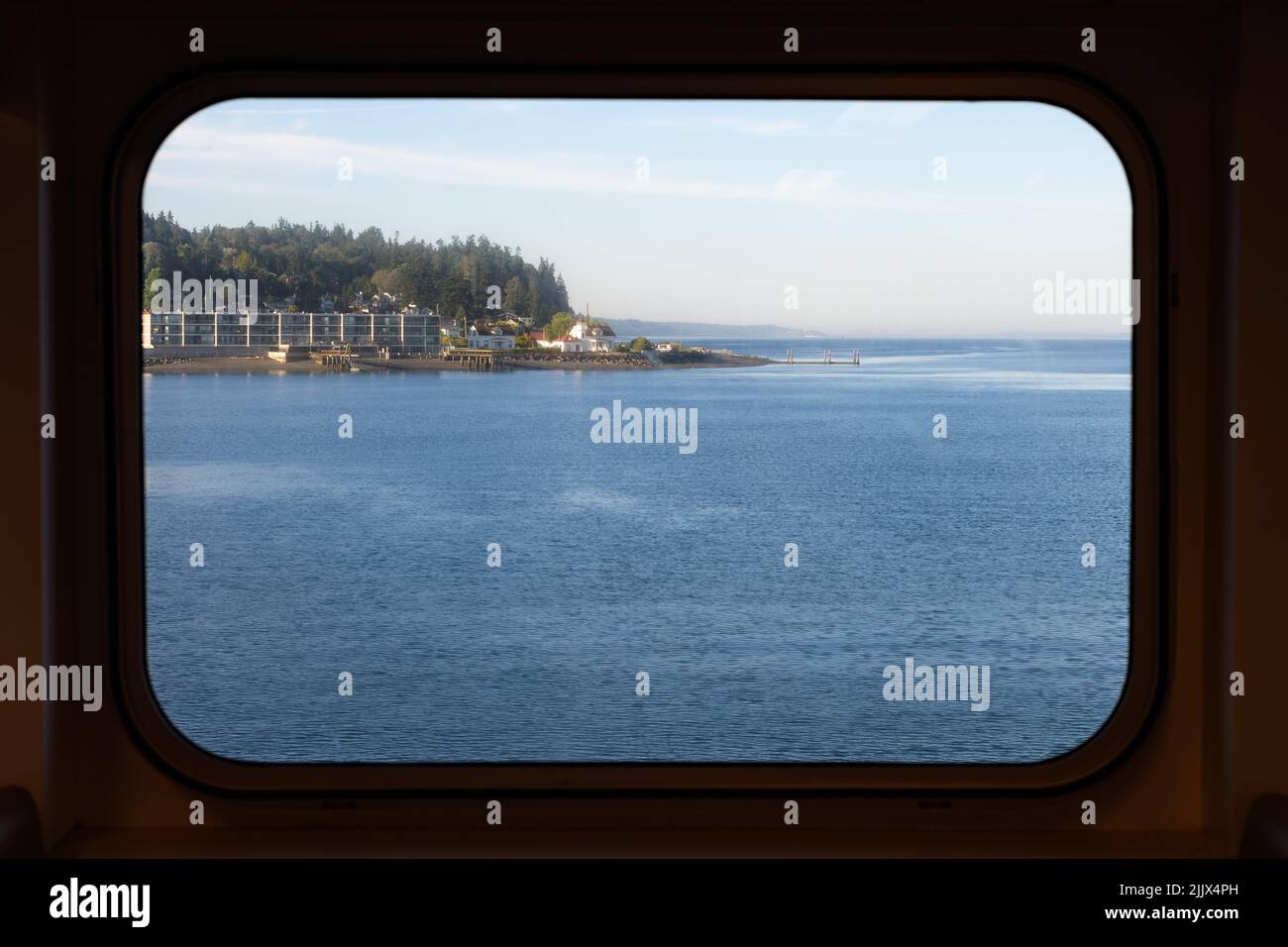 Blick durch ein rechteckiges Fährfenster auf die Küste von Mukilteo und das blaue Wasser des Puget Sound Stockfoto