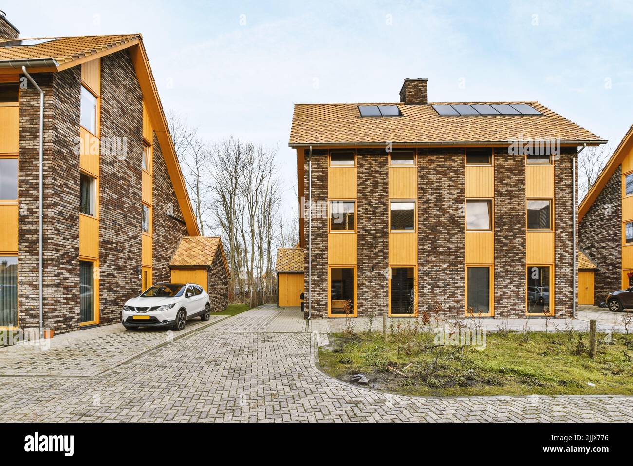 Moderne rustikale Backsteinhäuser mit einem Auto, das auf der Kopfsteinpflasterstraße geparkt ist Stockfoto
