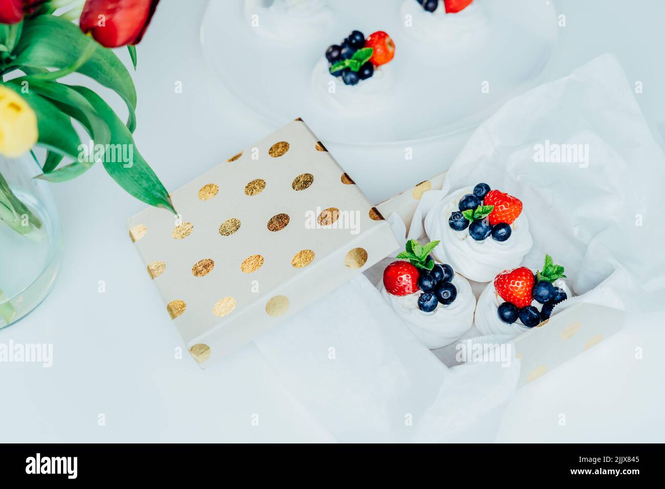 Set aus Pavlova-Baiser-Dessertkuchen mit frischen Erdbeeren und Blaubeeren, dekoriert mit Minze in Geschenkbox verpackt. Süße Präsens Idee. Festliche Foo Stockfoto