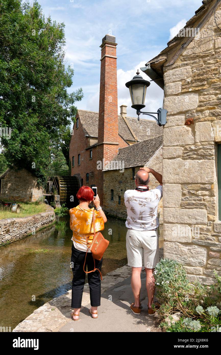 Touristen in den Cotswolds fotografieren die Alte Wassermühle am River Eye in Lower Slaughter. Die alte Mühle ist eine beliebte Besucherattraktion Stockfoto