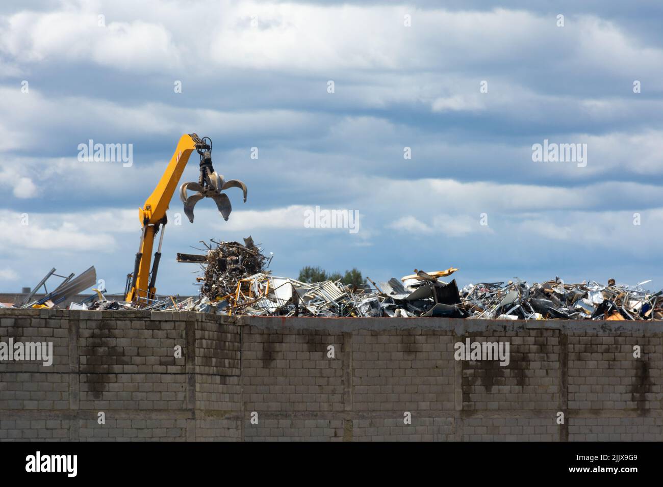 Kran mit Greifer, der Metallschrott in einer Metallabfallverarbeitungsanlage auf Berge von Schrott und Metallen ablässt Stockfoto