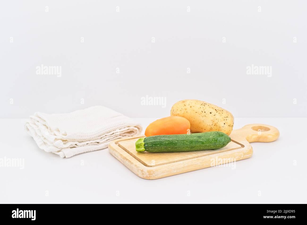 Frisches Gemüse aus biologischem Anbau auf einem hölzernen Schneidebrett mit weißem Küchentuch Stockfoto