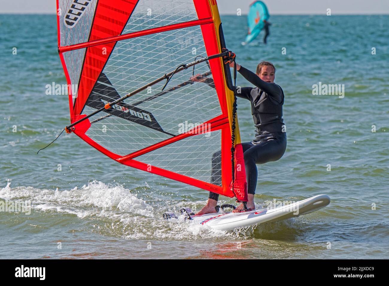 Mädchen / weibliche Freizeit Windsurfer in schwarzem Neoprenanzug üben klassischen Windsurfen auf See Stockfoto